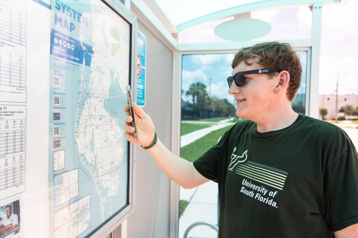 A young male USF student scanning a QR code at a PSTA bus shelter