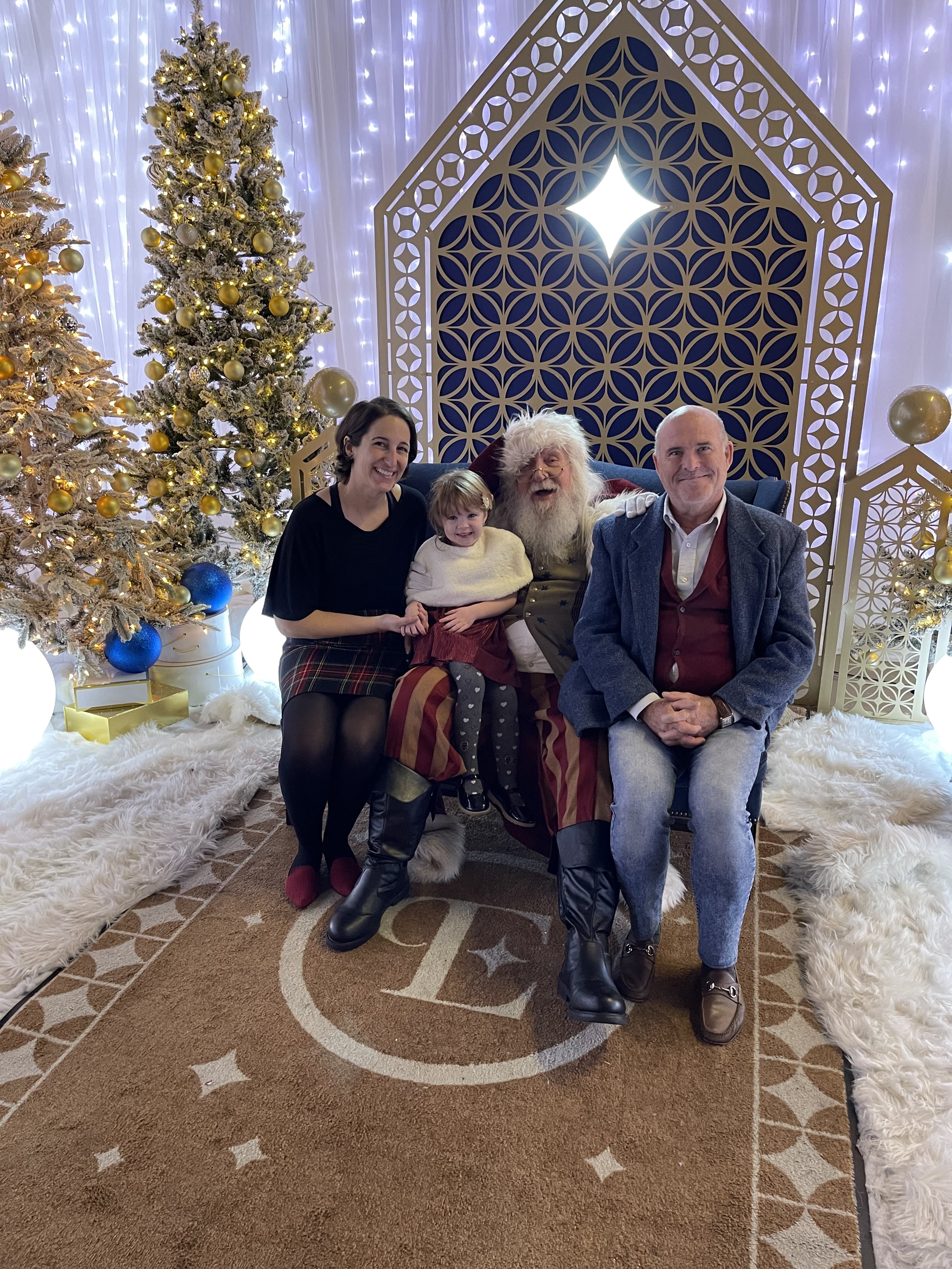 Julia, her husband, and daughter Emily sitting with Santa Claus at the St. Pete Enchant event.