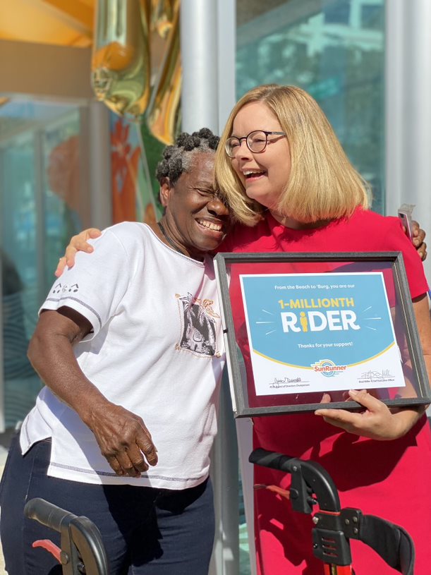 Photo of Gina Driscoll hugging Geneva Gibbs and presenting her with an award for being the one-millionth SunRunner rider
