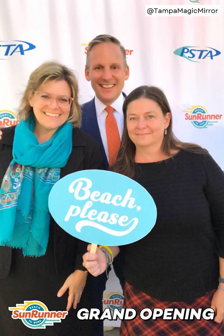 Photo of three people at the SunRunner grand opening holding the sign "Beach, please." Left to right: Cassandra Borchers, Brad Miller, and Heather Sobush