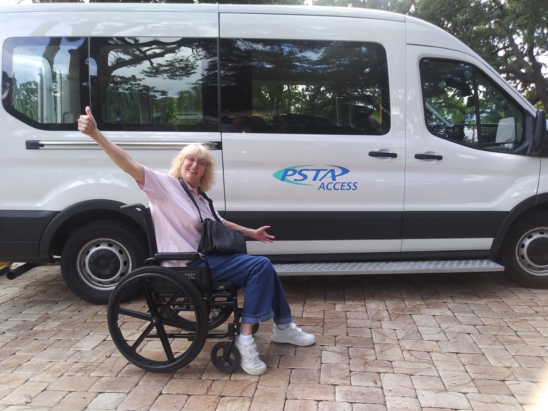 Kim Rankine, TRAC Member representing PSTA Access, in her wheelchair in front of an Access vehicle, holding her arms out and giving a thumbs up