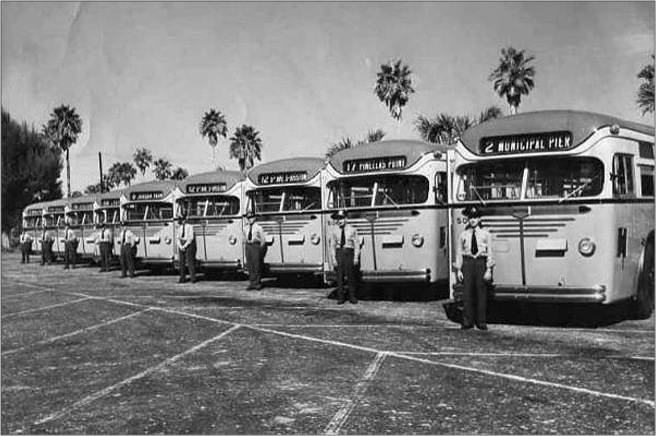 A black and white photo of a line of nine 50's era SPMTS buses with their operators standing in front of them