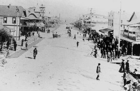 A black and white photo of Central Avenue in 1901, before roads or trolley tracks. People are walking around and bikes and horse-drawn carriages can be seen.