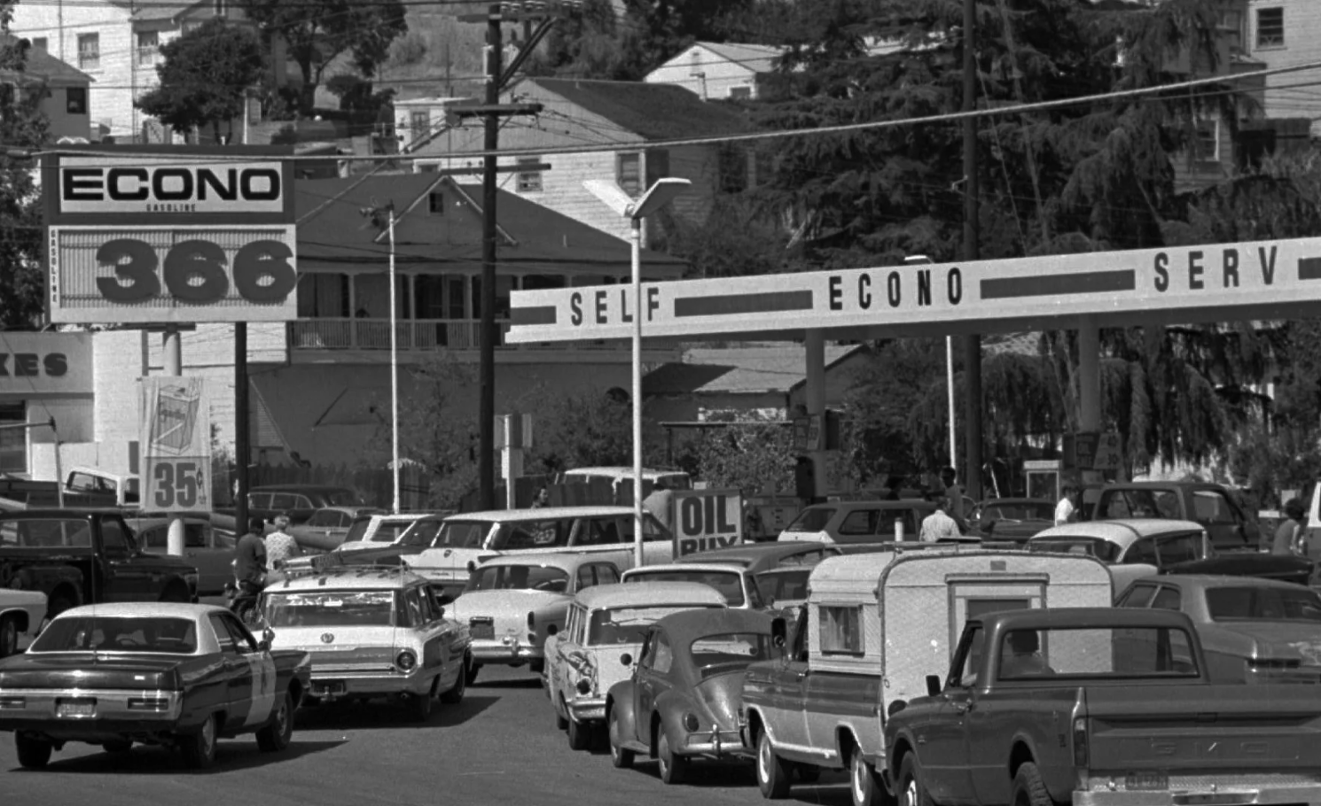 A black and white photo of 70s-era vehicles lining up at an Econo gas station in hopes of getting gas; the gas price is $3.66, which was very expensive for the time.