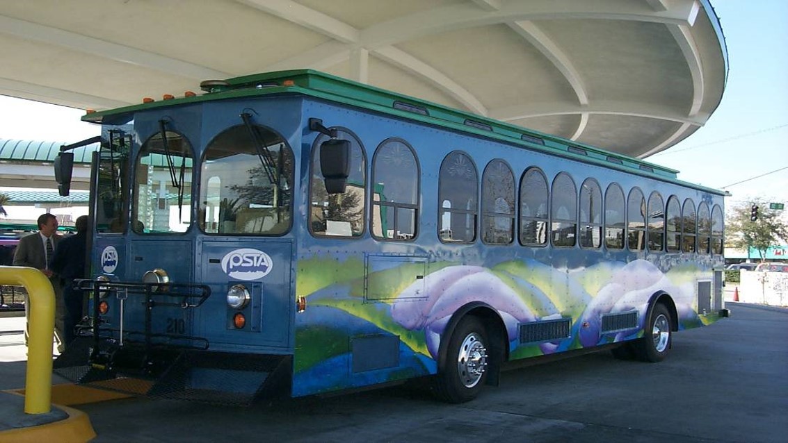 A photo of the unveiling for the Suncoast Beach Trolley, which is a blue trolley-style bus with purple and green designs on it.