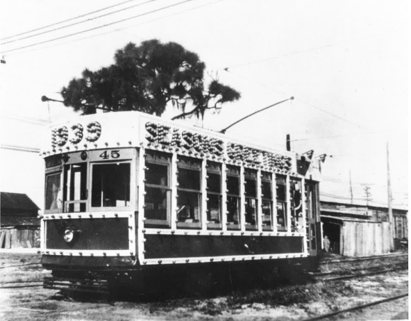 A black and white photo of a streetcar covered in light bulbs that spell out "1939 Seasons Greetings"