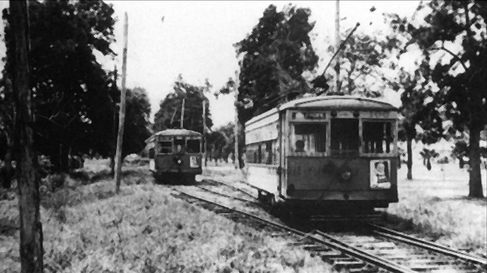 A black and white image of two trolleys; one is further back and waiting while the closer one enters the Gulfport Line track switch.