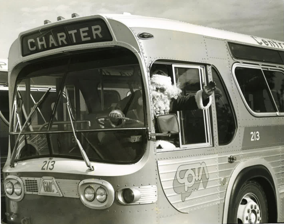 A black and white photo of a bus operator dressed as Santa Claus, leaning out the window of a CPTA bus to wave at the camera