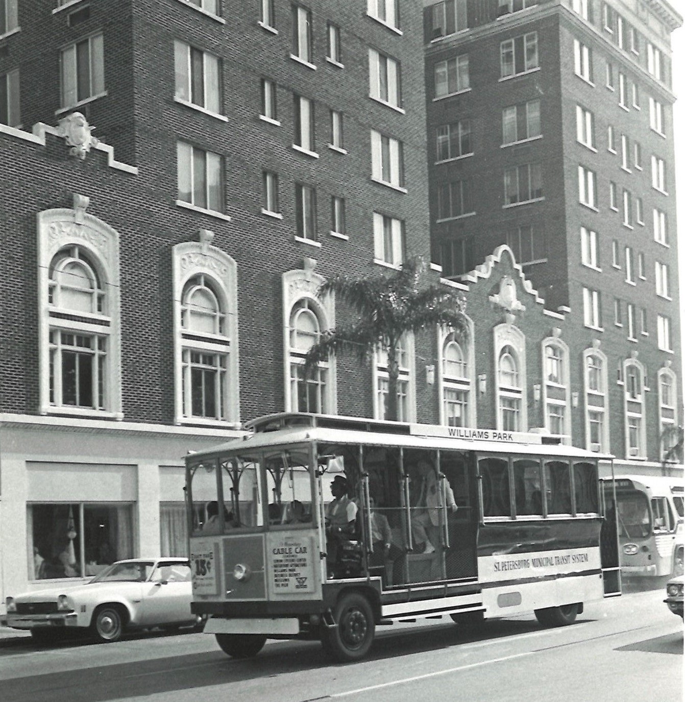 A black and white photo of an open-air, cable car-style bus driving past The Princess Martha hotel.