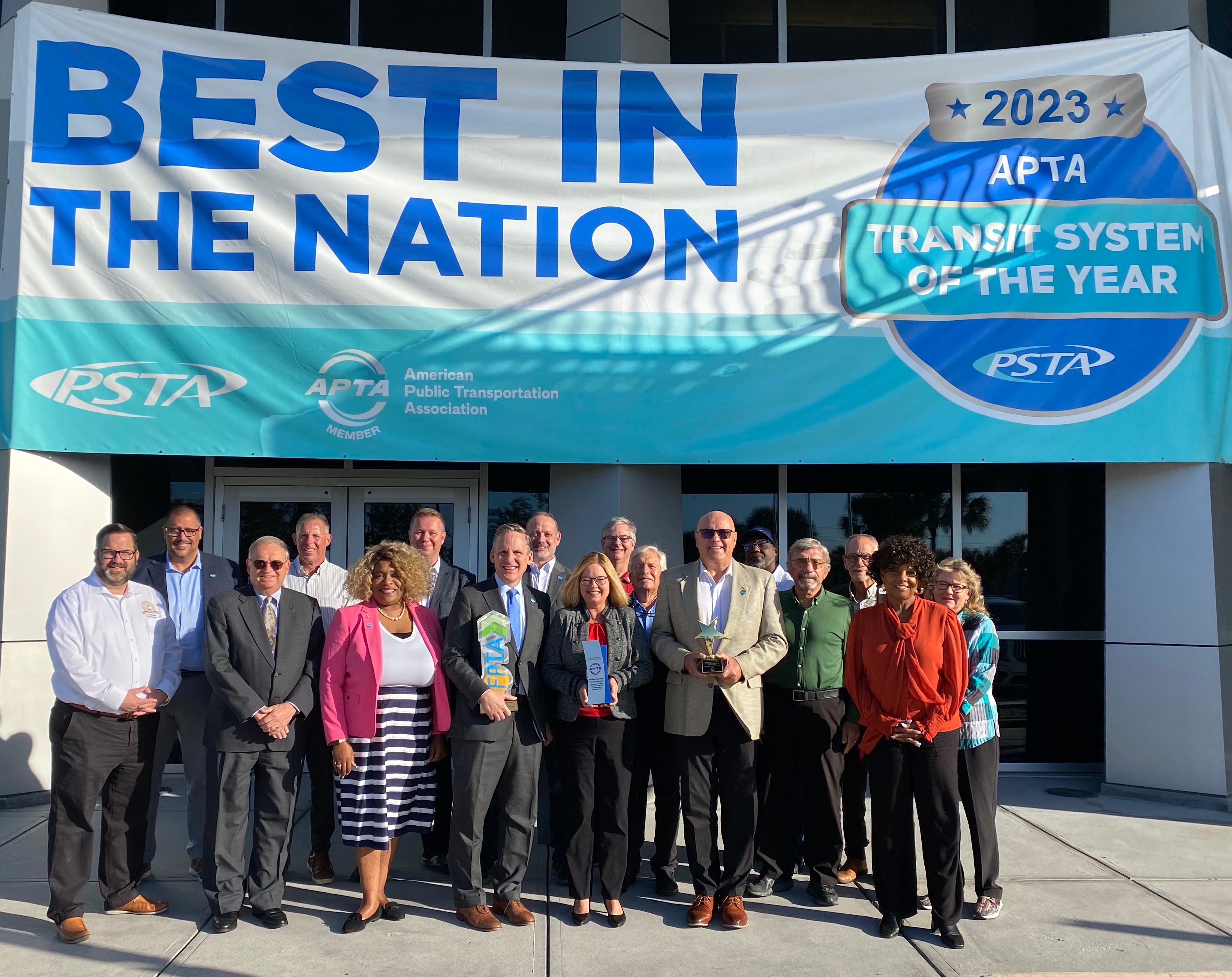 A photo of PSTA's Board of Directors holding PSTA's best in the state and nation awards, standing in front of a banner that says "Best in the Nation" with the APTA Transit System of the Year 2023 emblem.