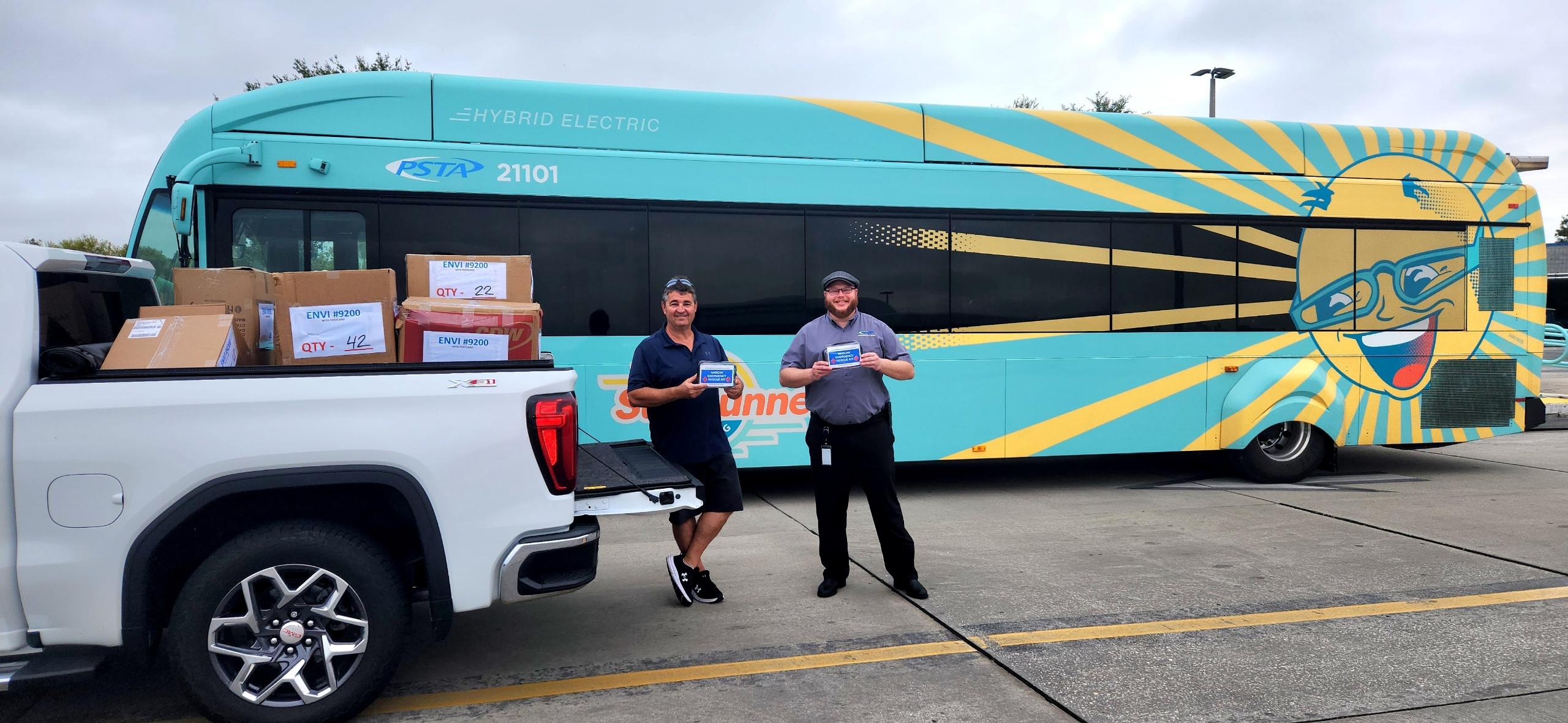 A photo of Dan Zsido and Eddie Kester in front of a SunRunner bus holding Narcan kits; in the foreground is a white pick-up truck with boxes full Narcan kits.