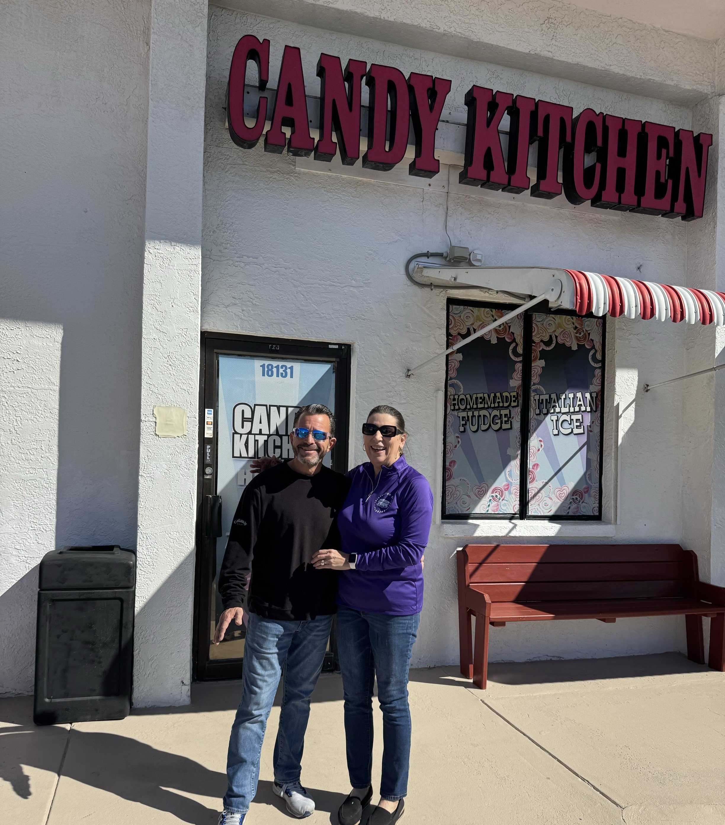 A photo of The Candy Kitchen owners Pam & Bob Hoffman standing outside the storefront.