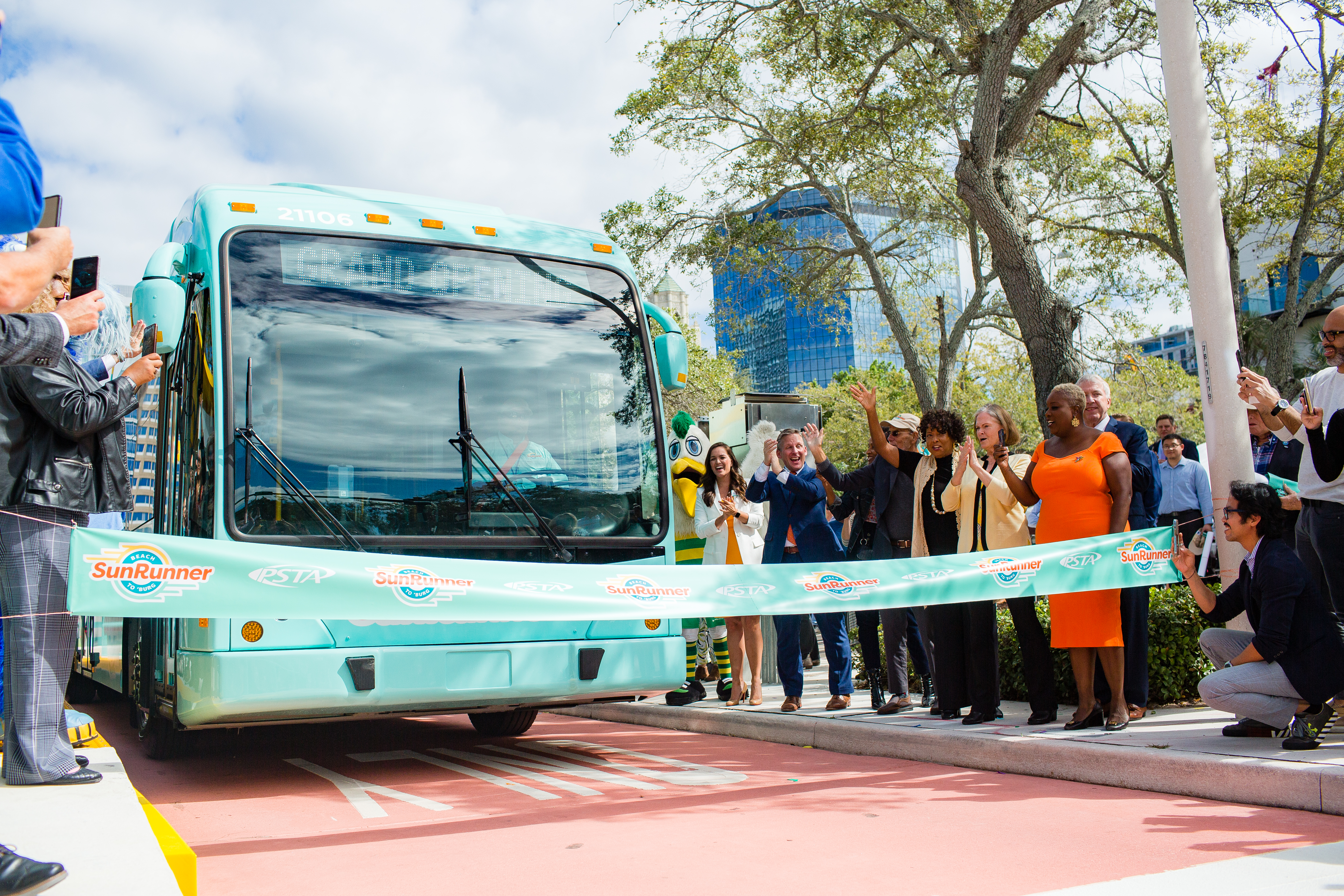 A photo of the SunRunner driving through a ribbon for the official launch of the SunRunner service. Onlookers stand on either side clapping in excitement.