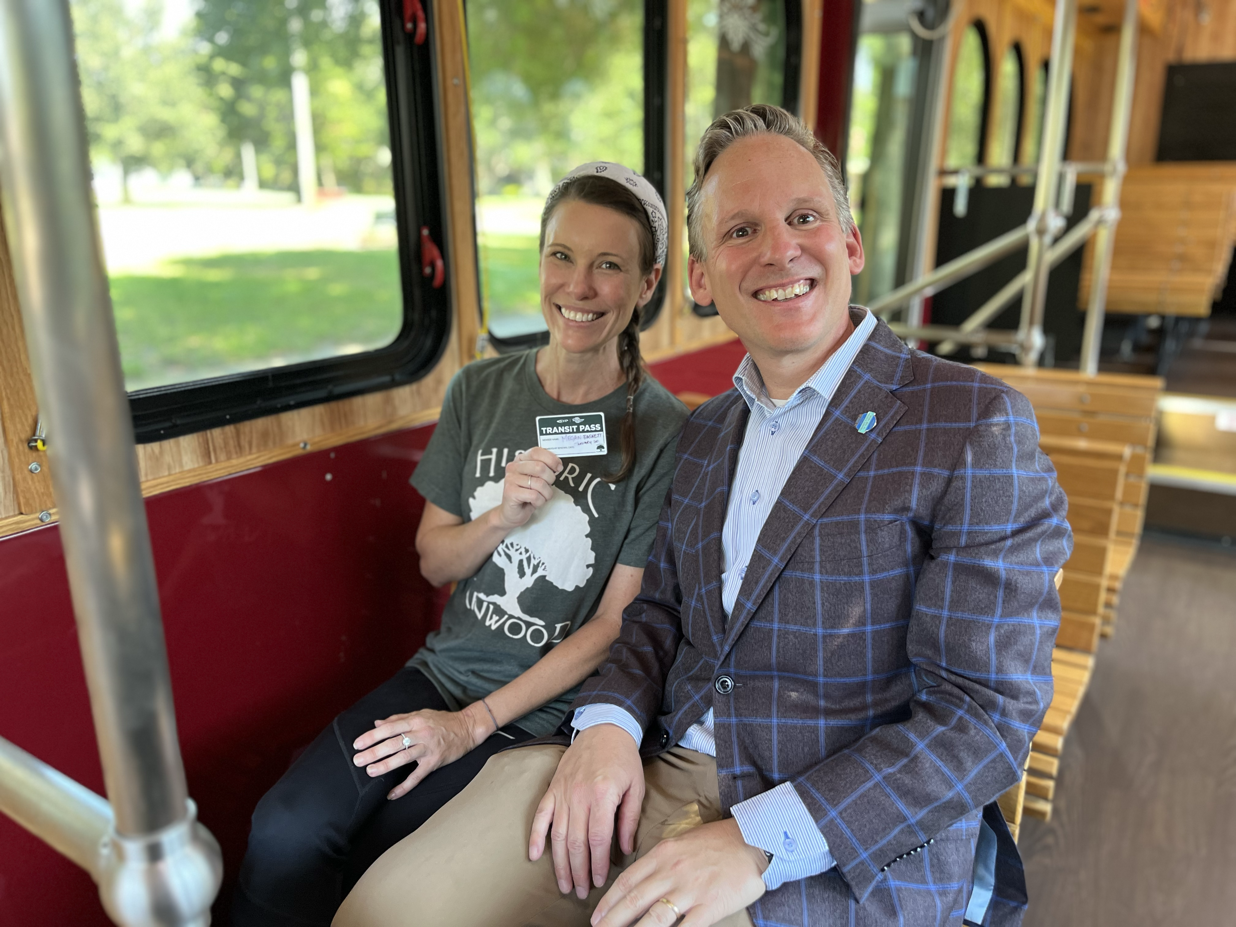 CEO Brad Miller and Historic Kenwood Neighborhood Association member Megan Basnett sit smiling on the trolley. Megan is holding a green and white bus pass, the very first one of the neighborhood's UPASS program.
