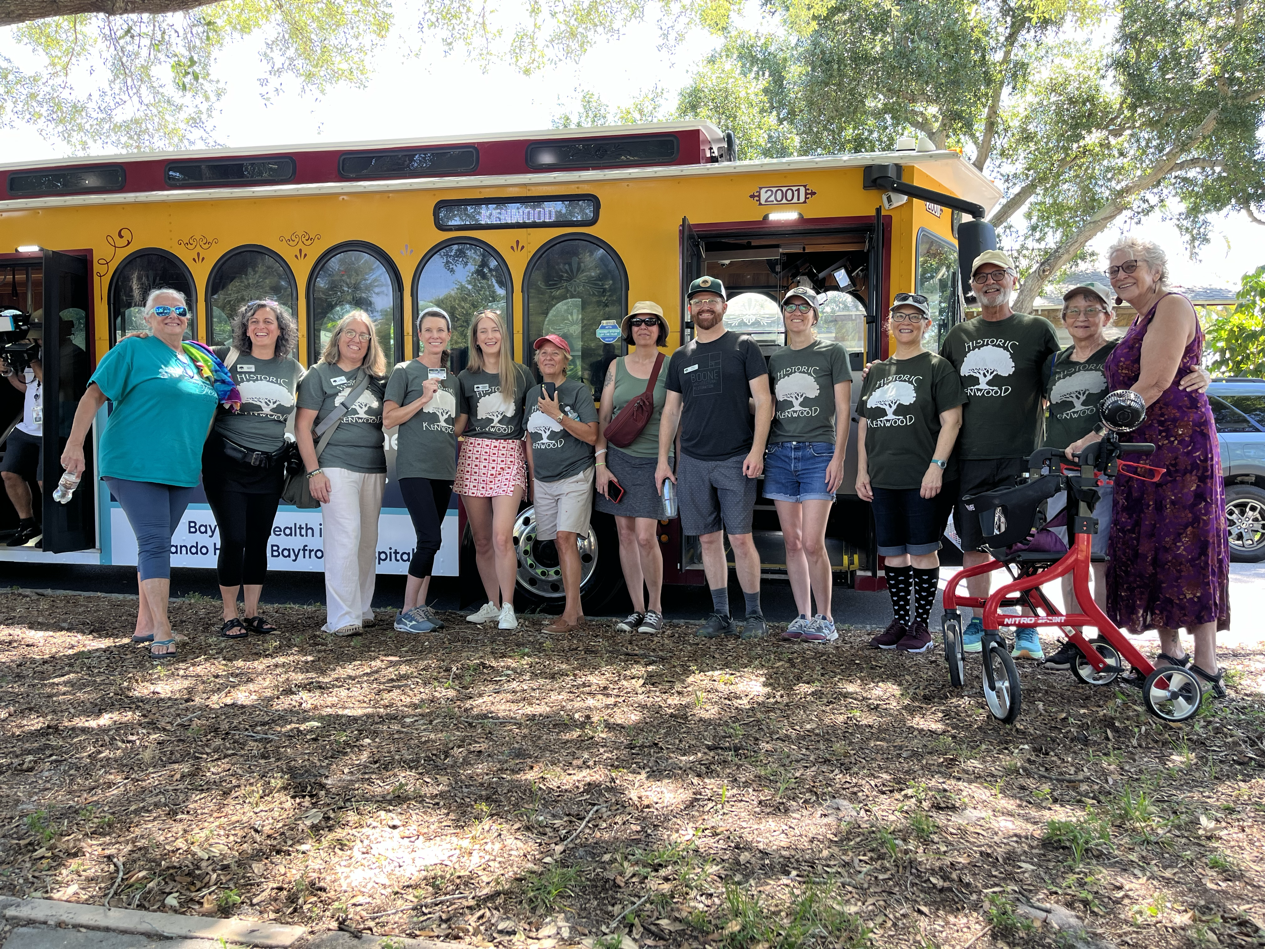 A group of 13 people stand in front of a yellow and red trolley. These are members for the Historic Kenwood Neighborhood Association celebrating the launch of their neighborhood's UPASS program.