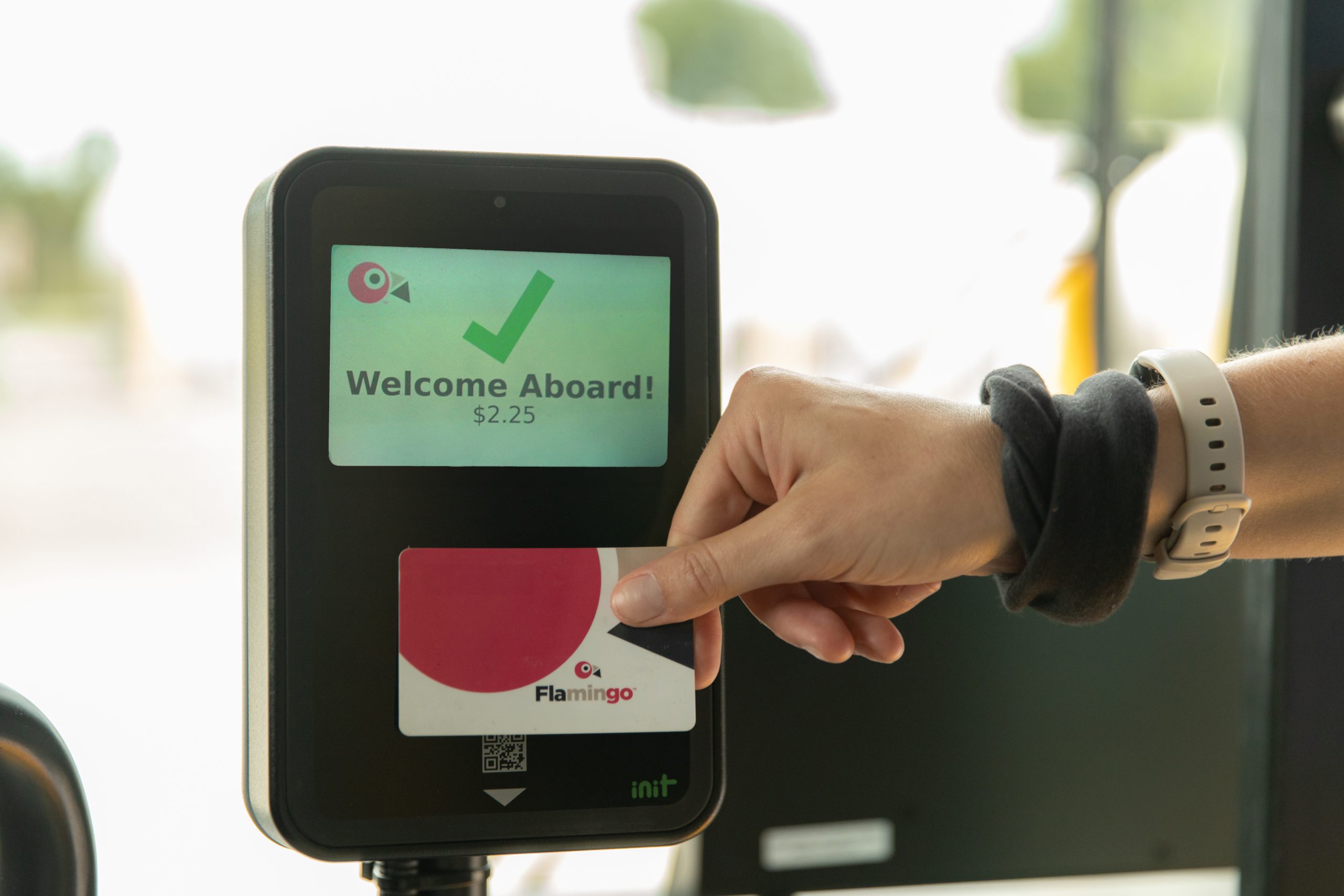 Close up of hand tapping with a flamingo card on fare box and message on fare machine says Welcome Aboard
