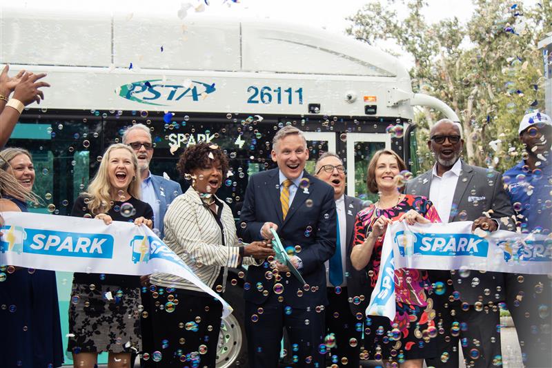A photo of PSTA's CEO Brad Miller and community leaders holding a Spark-branded ribbon as it's cut with oversized scissors.