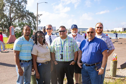 A group of seven people from safety, security, and training, and other operations departments, standing by the water.