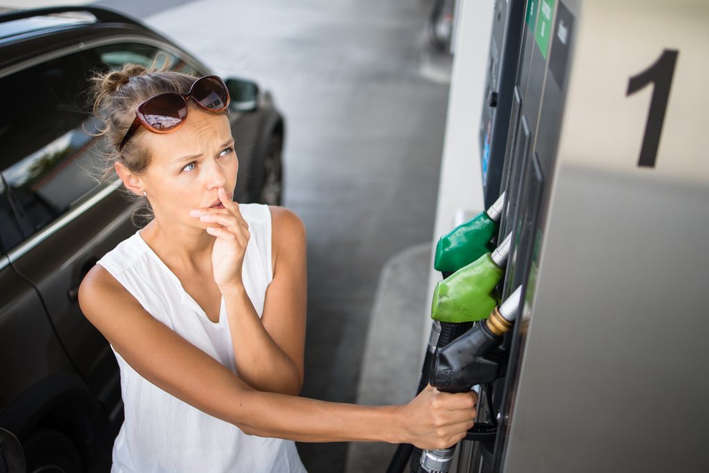 A woman reaching for a gas pump nozzle with a look of anxiety on her face over high gas prices.
